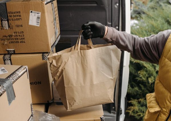 pexels-photo-6407565 A courier handling packages and paper bags in a van for delivery service.